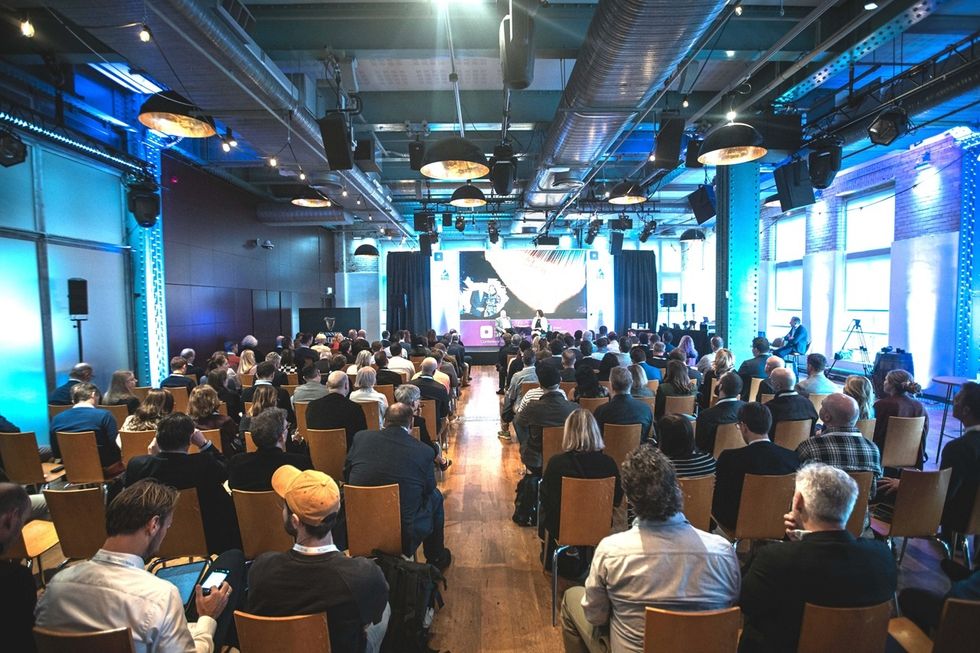 Audience seated in a modern conference room with a presenter on stage.