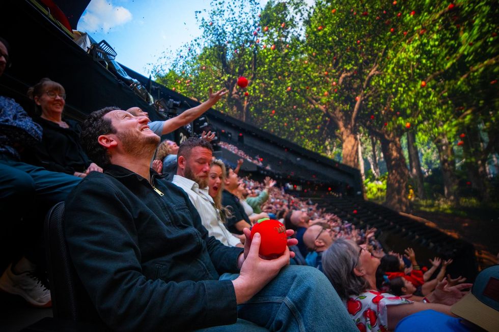 Audience tosses red apples in the Sphere venue with a digital forest projection.