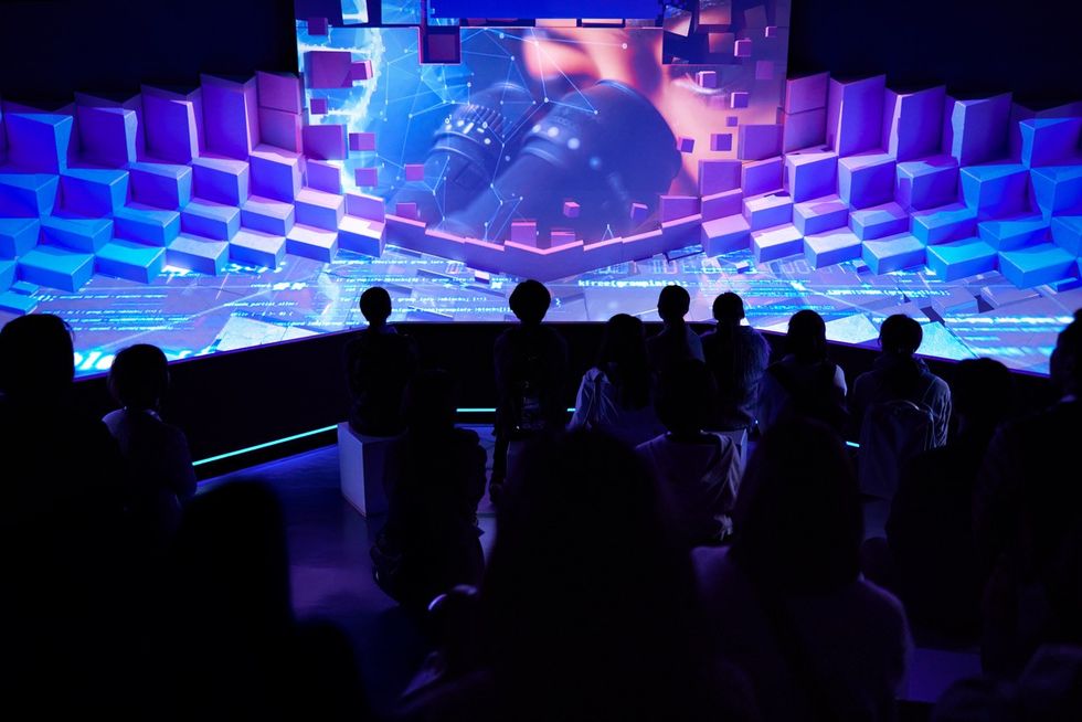 Audience watches a colorful, immersive digital projection in a dark room.