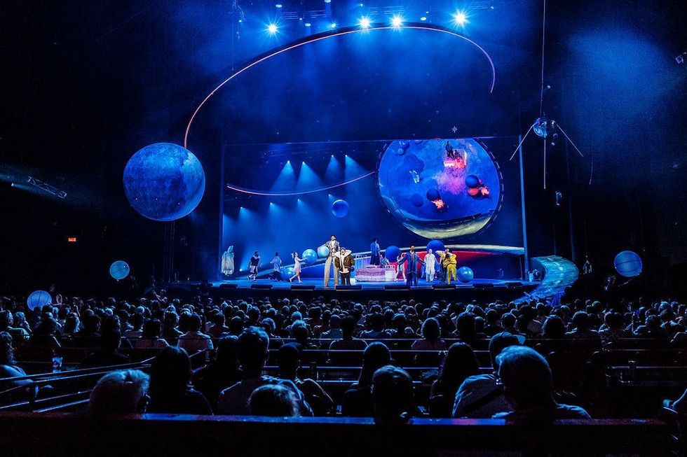 Audience watching a cosmic-themed Cirque du Soleil stage performance with blue lighting.