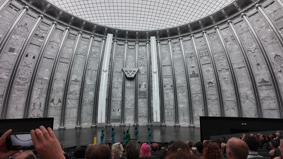 Audience watching a performance in a vast, futuristic Cosm dome with intricate wall designs.