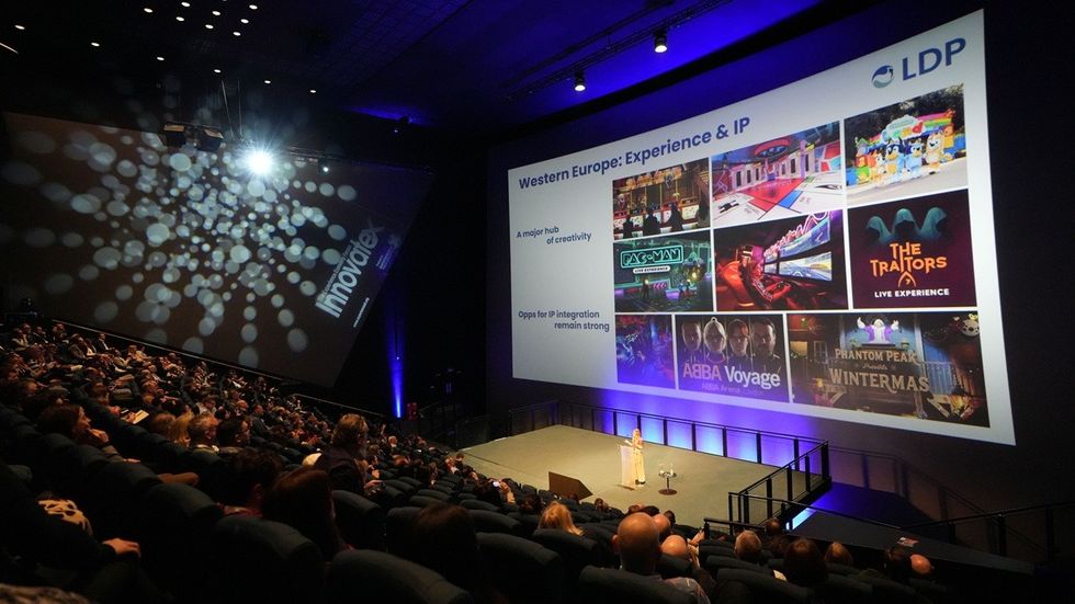 Audience watching a presentation on a large screen in a dimly lit auditorium.
