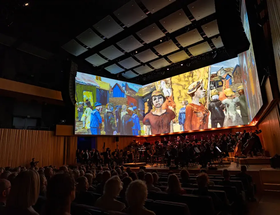 Audience watching orchestra with large Van Gogh-inspired art projection overhead.