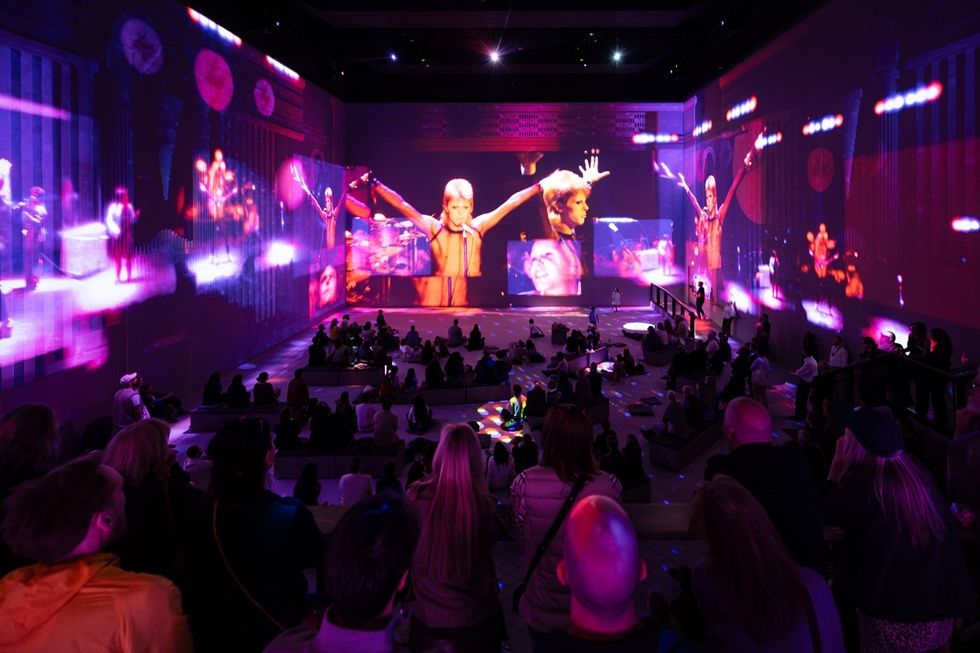 Audience watching vibrant light show on large, immersive screens.