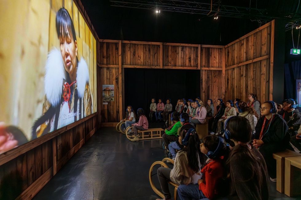 Audience with headphones watching a large screen in a dark wooden room in the Polar Experience immersive attraction.