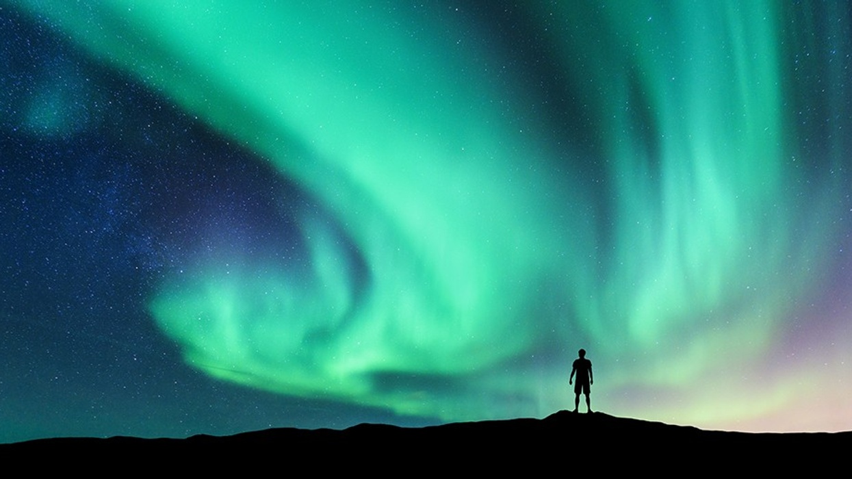 Aurora borealis and silhouette of standing man. Sky with stars and green polar lights.