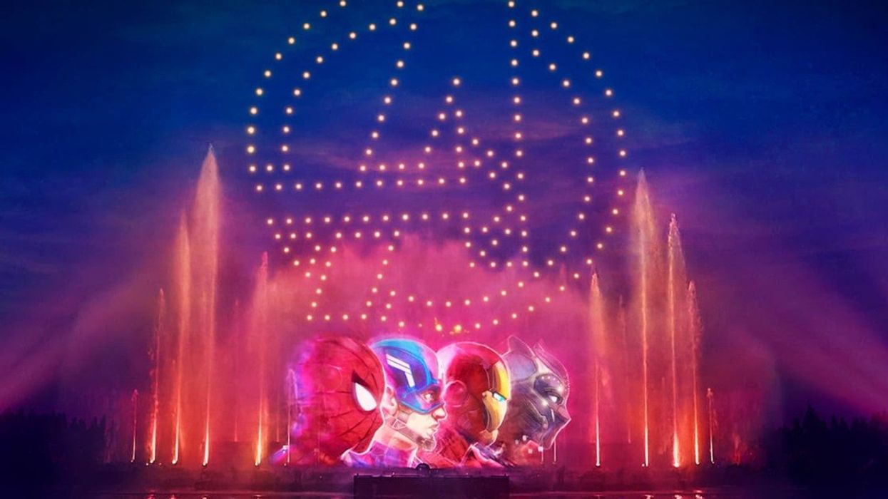 Avengers light show with character heads and logo above colorful fountains at night.