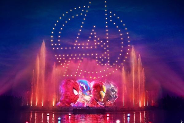 Avengers light show with character heads and logo above colorful fountains at night.