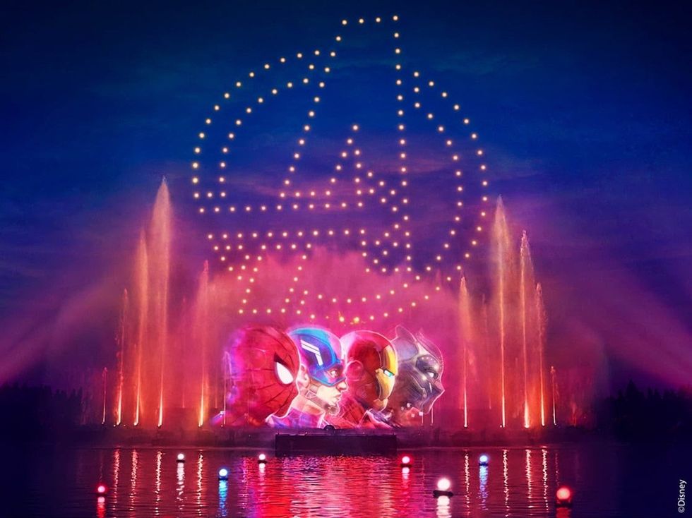 Avengers light show with character heads and logo above colorful fountains at night.