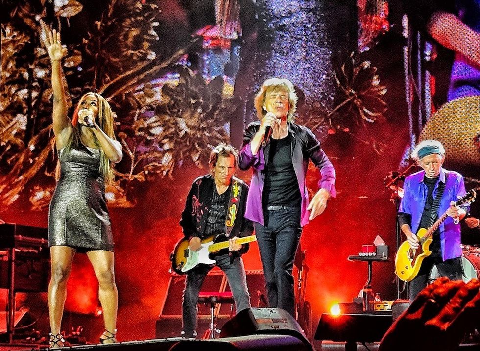 Band performing energetically on stage with vibrant lighting and backdrop.