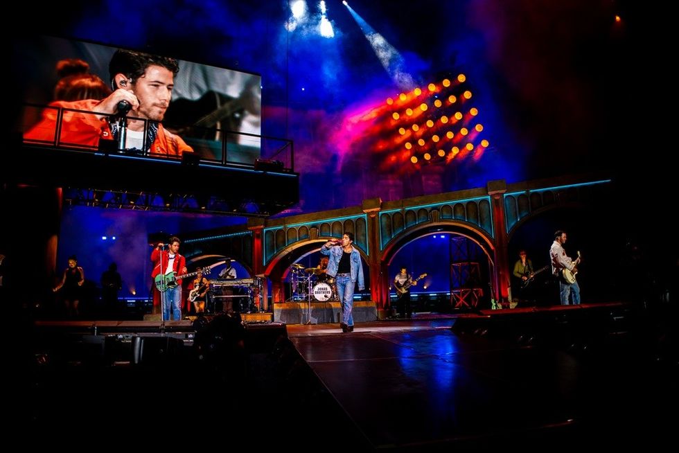 Band performing on a vibrant stage with colorful lights and a large screen backdrop.