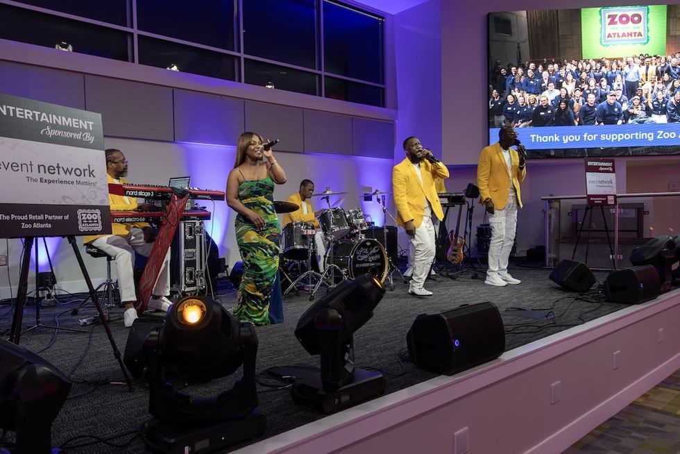 Band performing on stage with screens displaying "Zoo Atlanta" and audience photo.