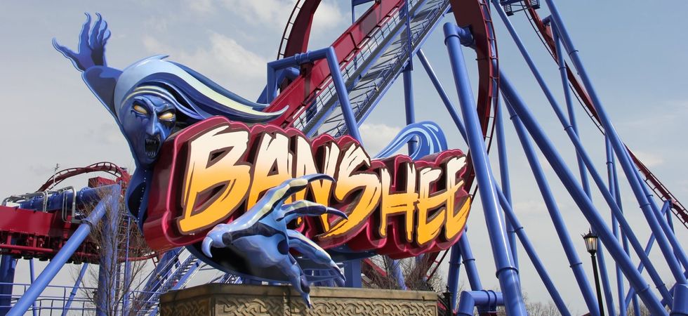 Banshee roller coaster entrance with a ghostly figure and looping tracks in the background at Kings Island