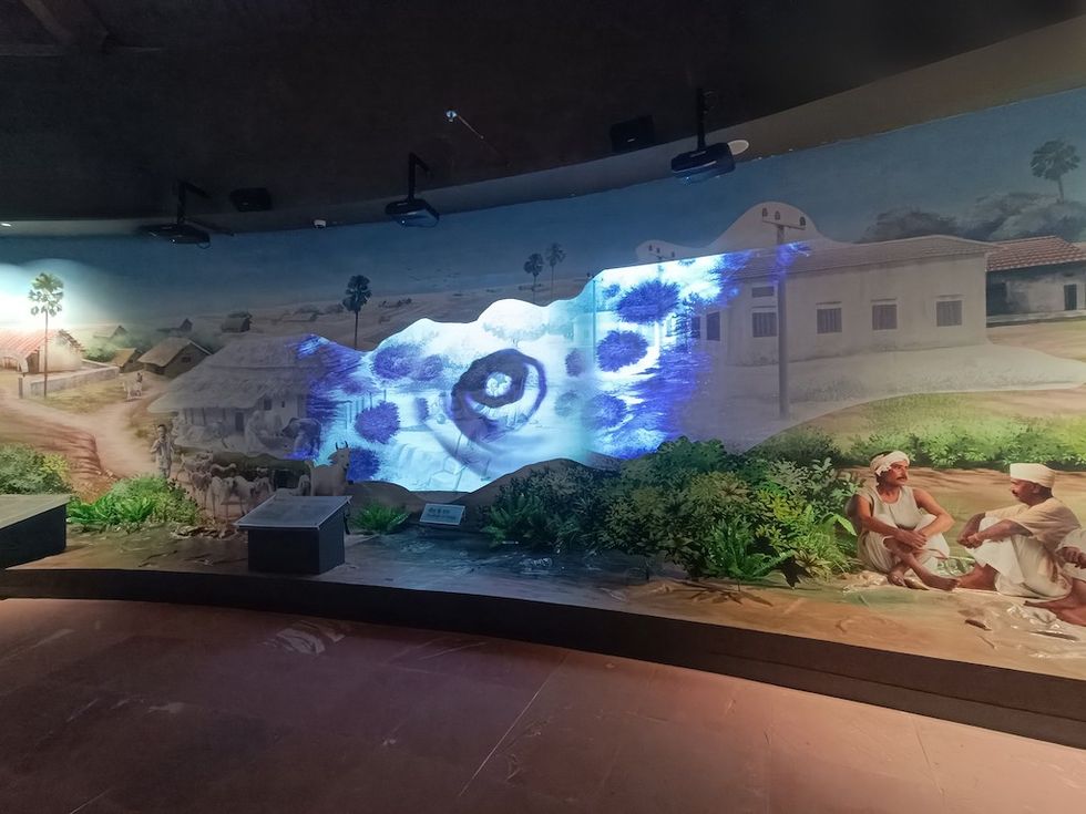 Bapu Tower Museum exhibit with a village mural and colorful projection display.