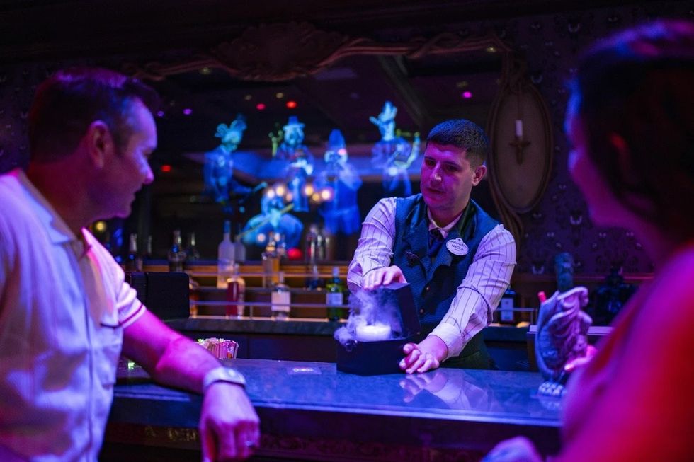 Bartender serving drinks with ghostly figures in the background at a themed bar.