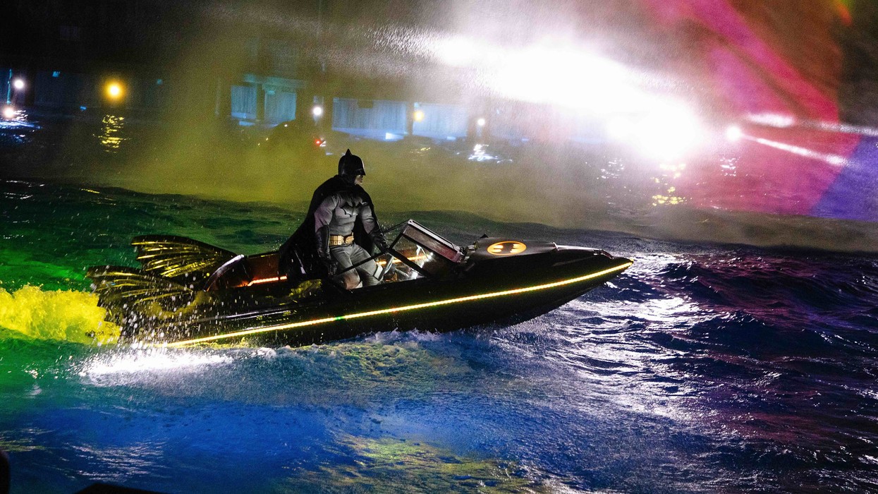 Batman on a lit-up speedboat in colorful, illuminated waters at night.