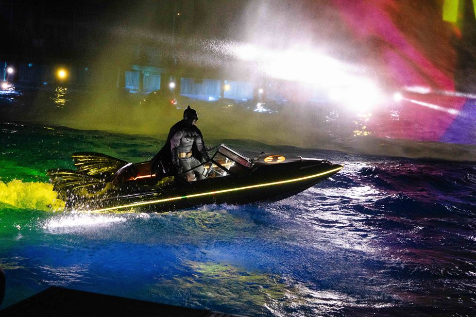 Batman on a lit-up speedboat in colorful, illuminated waters at night.