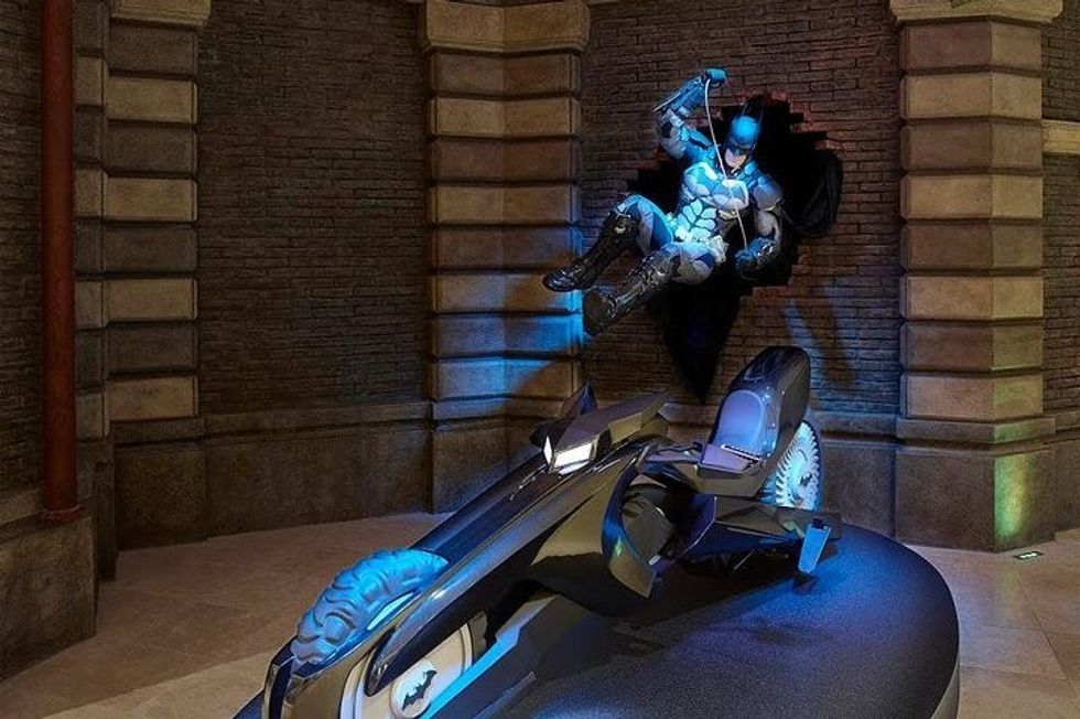 Batman statue bursting through wall on motorcycle display.