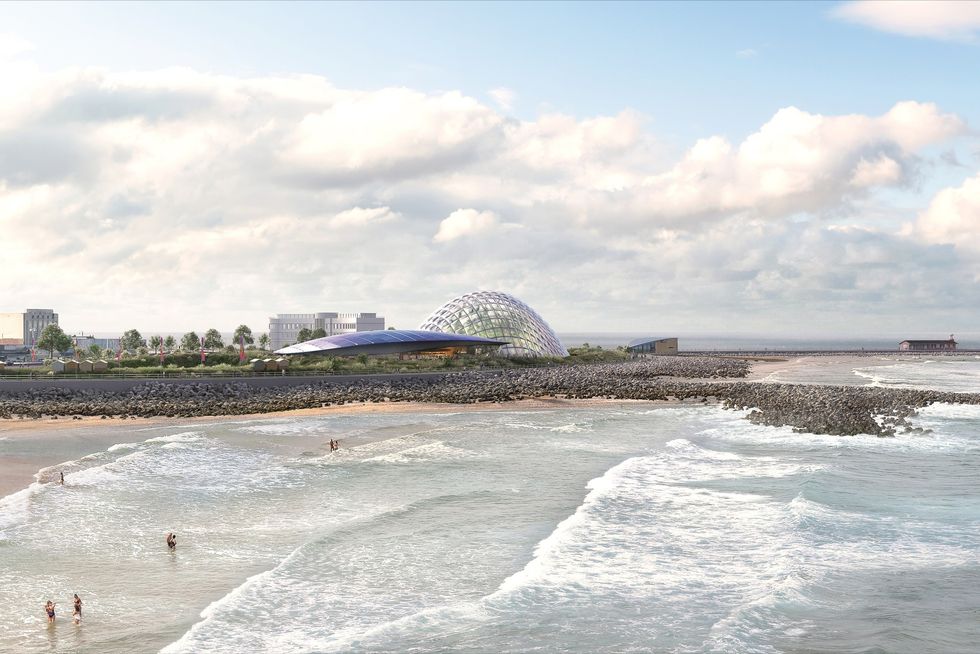 Beach with swimmers, rocky shoreline, and a futuristic dome-shaped building called Eden Project Morecambe in the background.