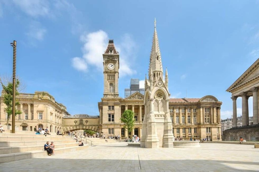 Birmingham Museum & Art Gallery sits in a historic city square with clock tower, ornate buildings, and a spired monument on a sunny day.