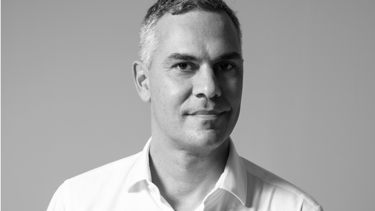 Black and white portrait of a man called Massimiliano Gioni in a white shirt, looking at the camera.