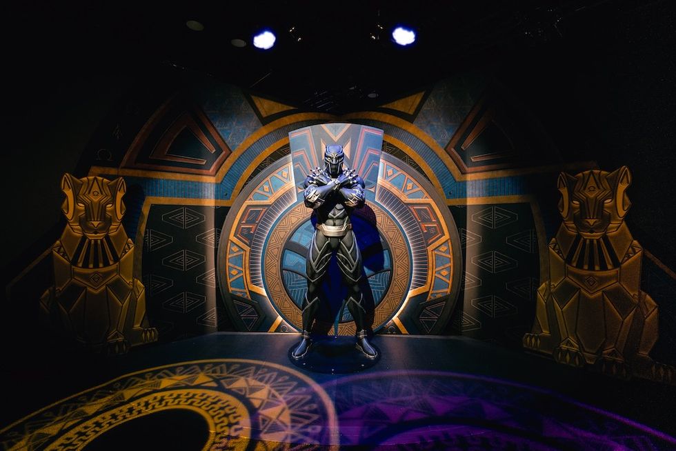 Black Panther statue with crossed arms, ornate backdrop, flanked by two gold panther sculptures.