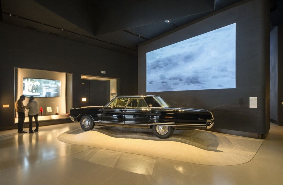 Black vintage car displayed in a dimly lit museum room with projected images at Zayed National Museum.
