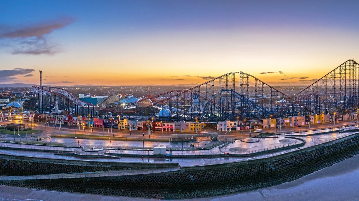 Blackpool Pleasure Beach at sunset, featuring a large roller coaster and brightly lit buildings.