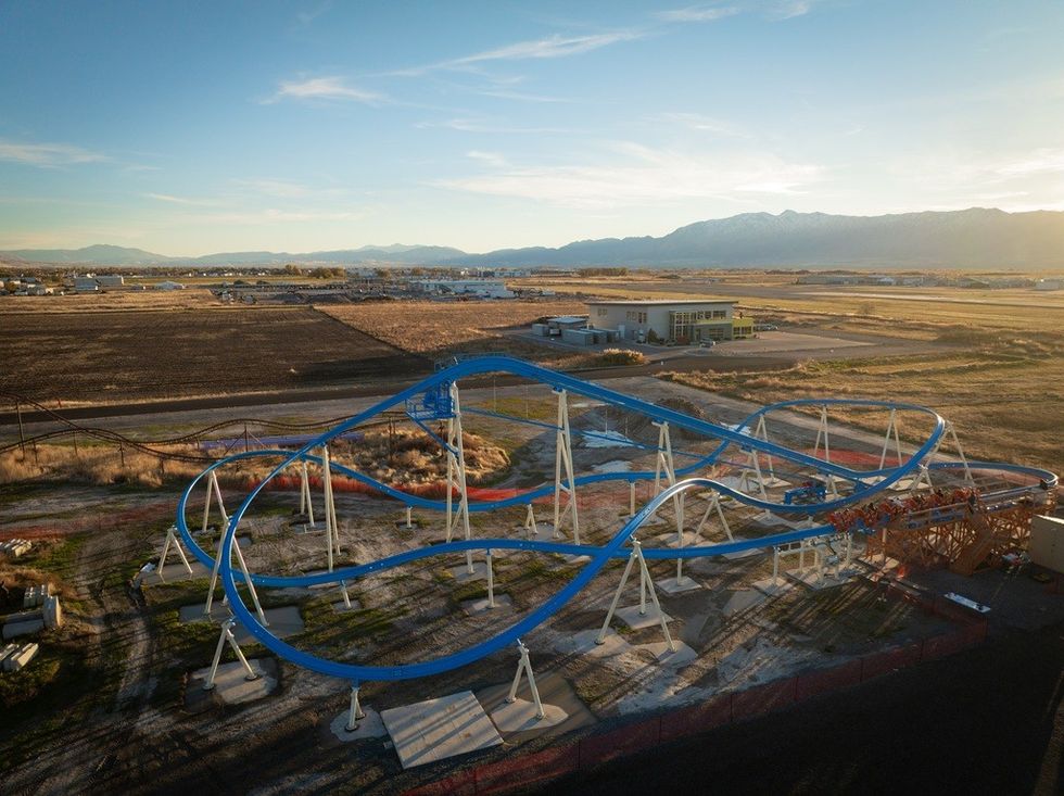 Blue and white roller coaster structure on a flat, rural landscape with mountains in the distance.