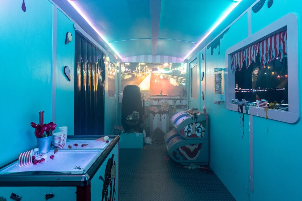 Blue-lit room with carnival-themed decor and cluttered surfaces.