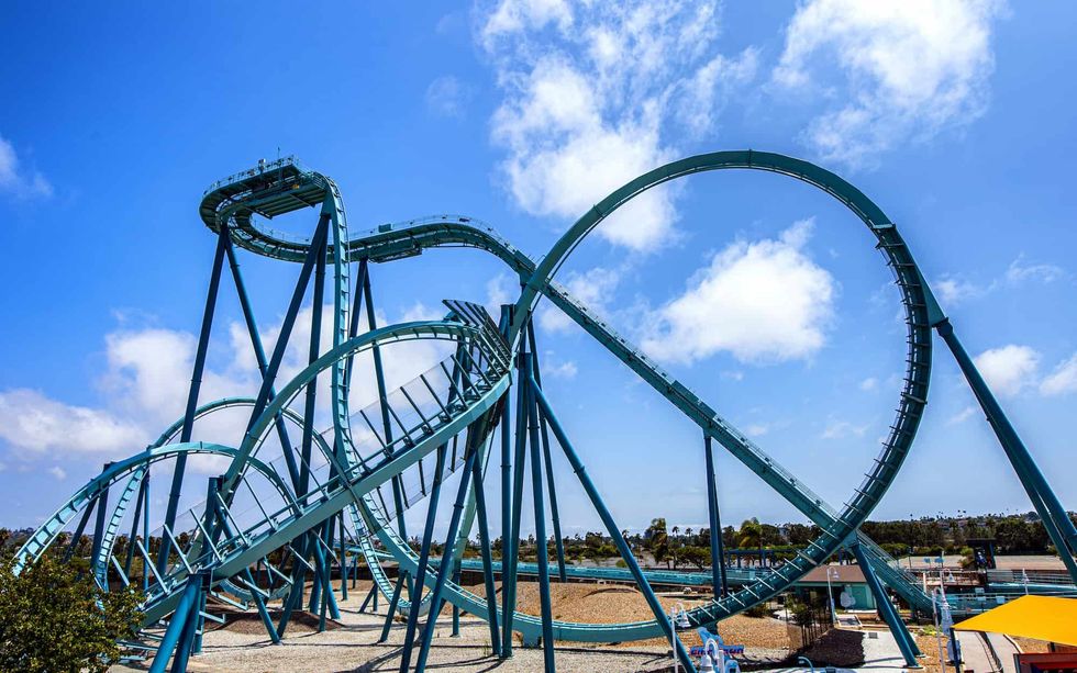 Blue roller coaster with loops under a bright blue sky.