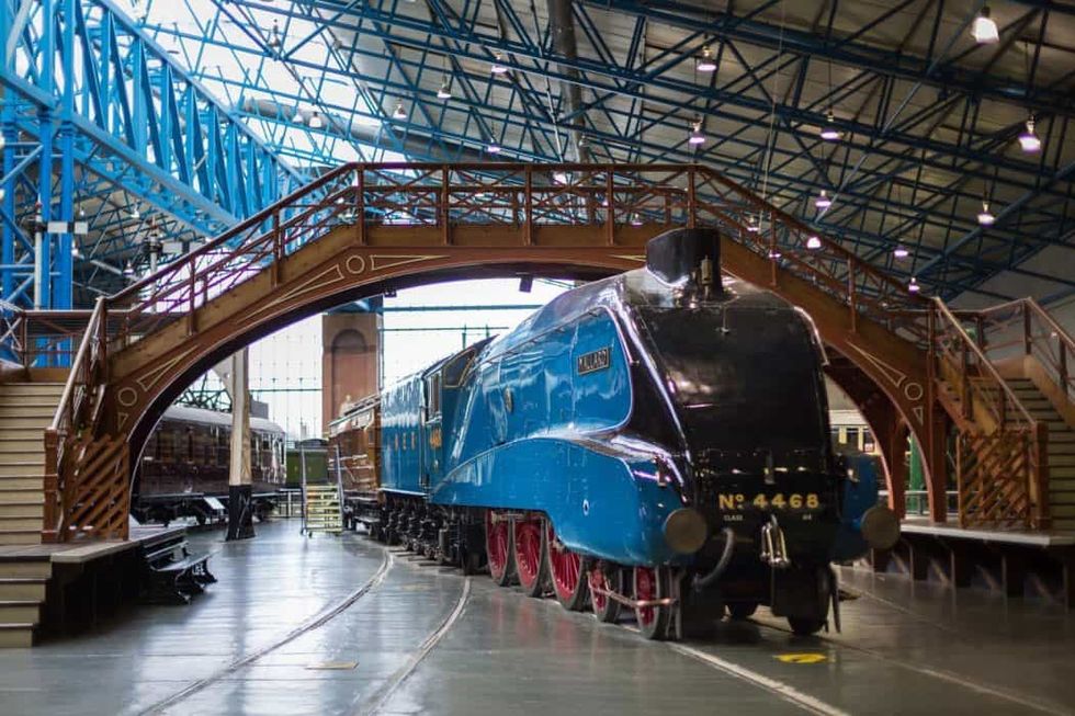 Blue steam locomotive under a wooden bridge in a museum setting at National Railway Museum York