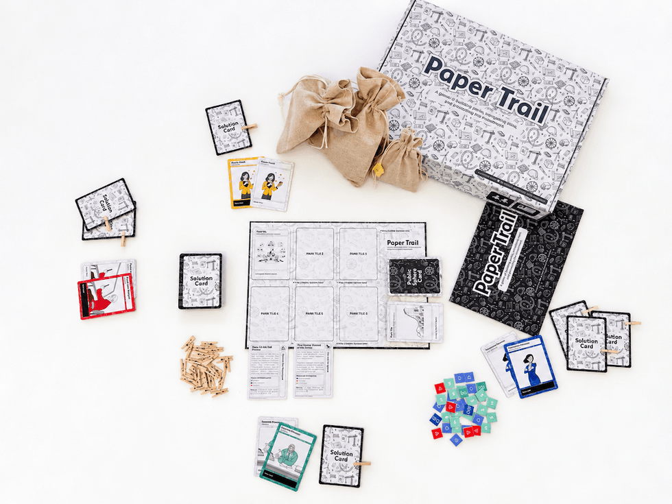 Board game setup with cards, tiles, tokens, cloth bags, and a box labeled "Paper Trail."