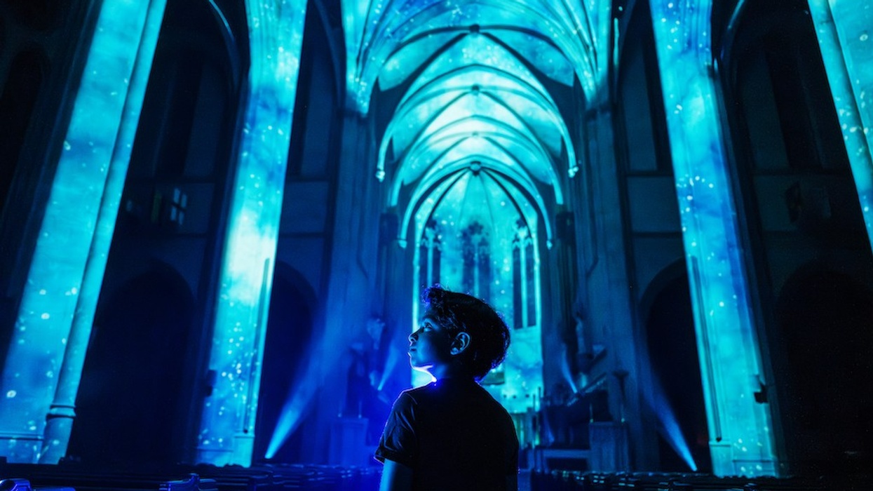 Boy in illuminated cathedral, blue light projection on arches and ceiling.