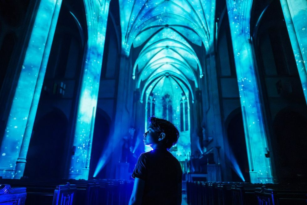 Boy in illuminated cathedral, blue light projection on arches and ceiling.