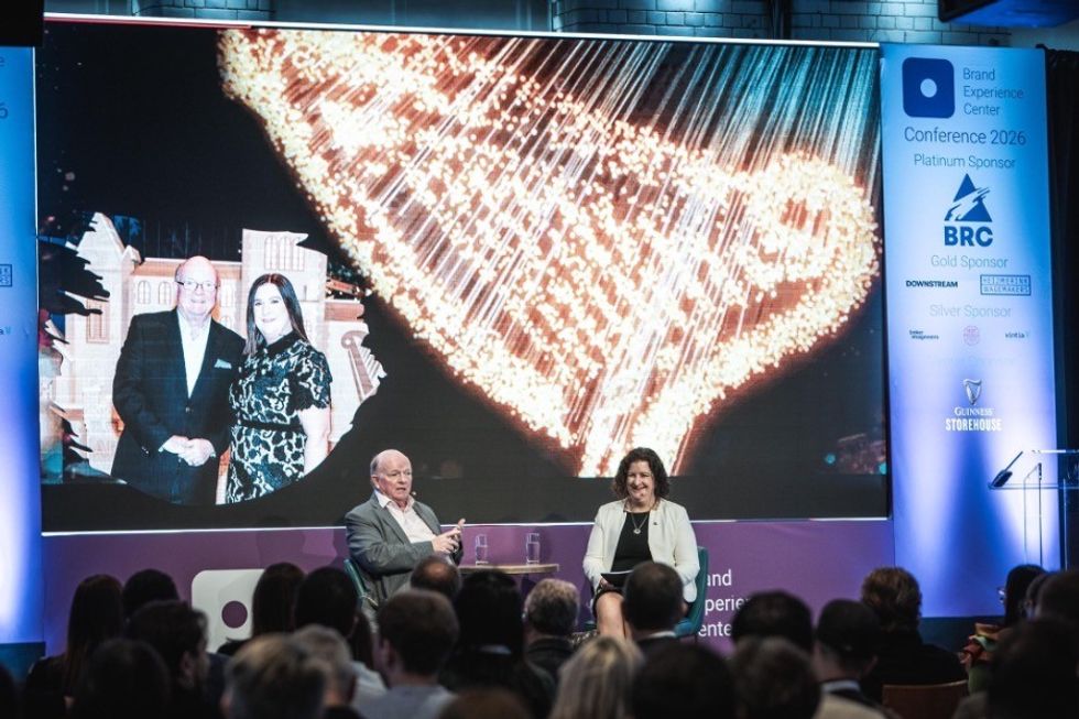 Brand Experience Center Conference panel discussion with a large screen and audience in a dimly lit room, Catherine Toolan and Paul Carty on stage