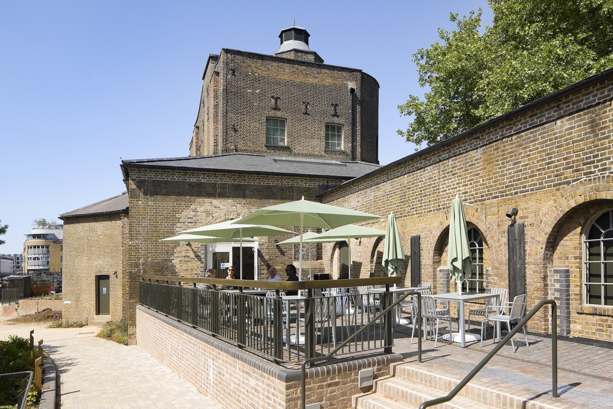 Brick building called the Quentin Blake Centre for Illustration with outdoor seating, green umbrellas, sunny day.