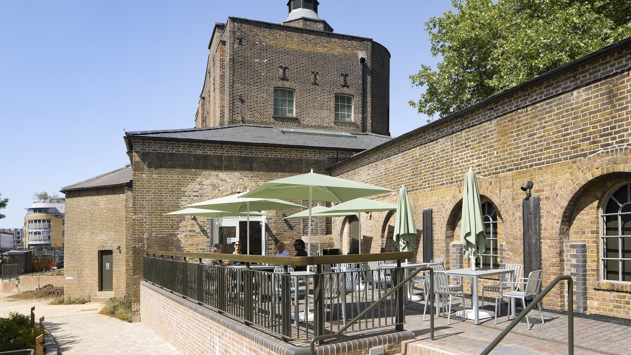 Brick building called the Quentin Blake Centre for Illustration with outdoor seating, green umbrellas, sunny day.