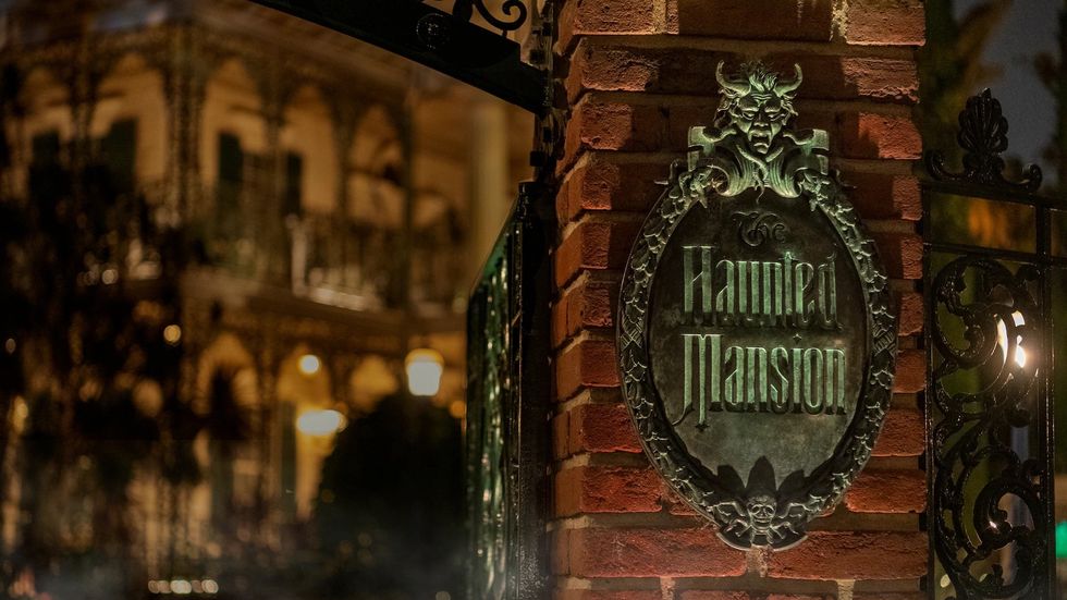 Brick column with "The Haunted Mansion" sign, dimly lit grand house in background.