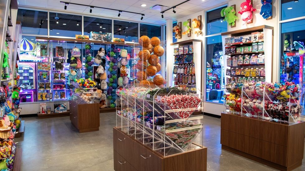 Bright arcade prize shop with plush toys, candy, and sports balls on display.