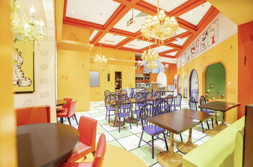 Bright, colourful cafe at Nickelodeon Playtime 2.0, with yellow walls, chandeliers, purple chairs, and comic-style artwork.