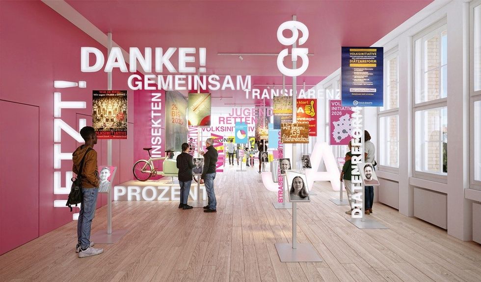 Bright room with pink walls, large text signs, posters, and people interacting.