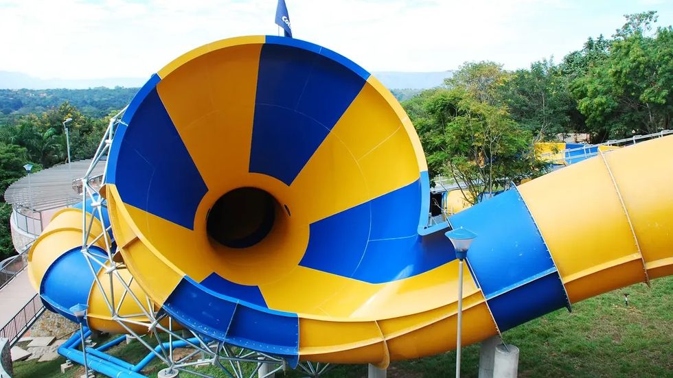 Bright yellow and blue water slide at Piscilagowith large funnel shape, surrounded by trees.