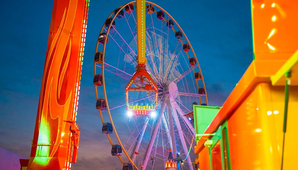 Brightly lit Ferris wheel and fairground ride at twilight at GLobal Village