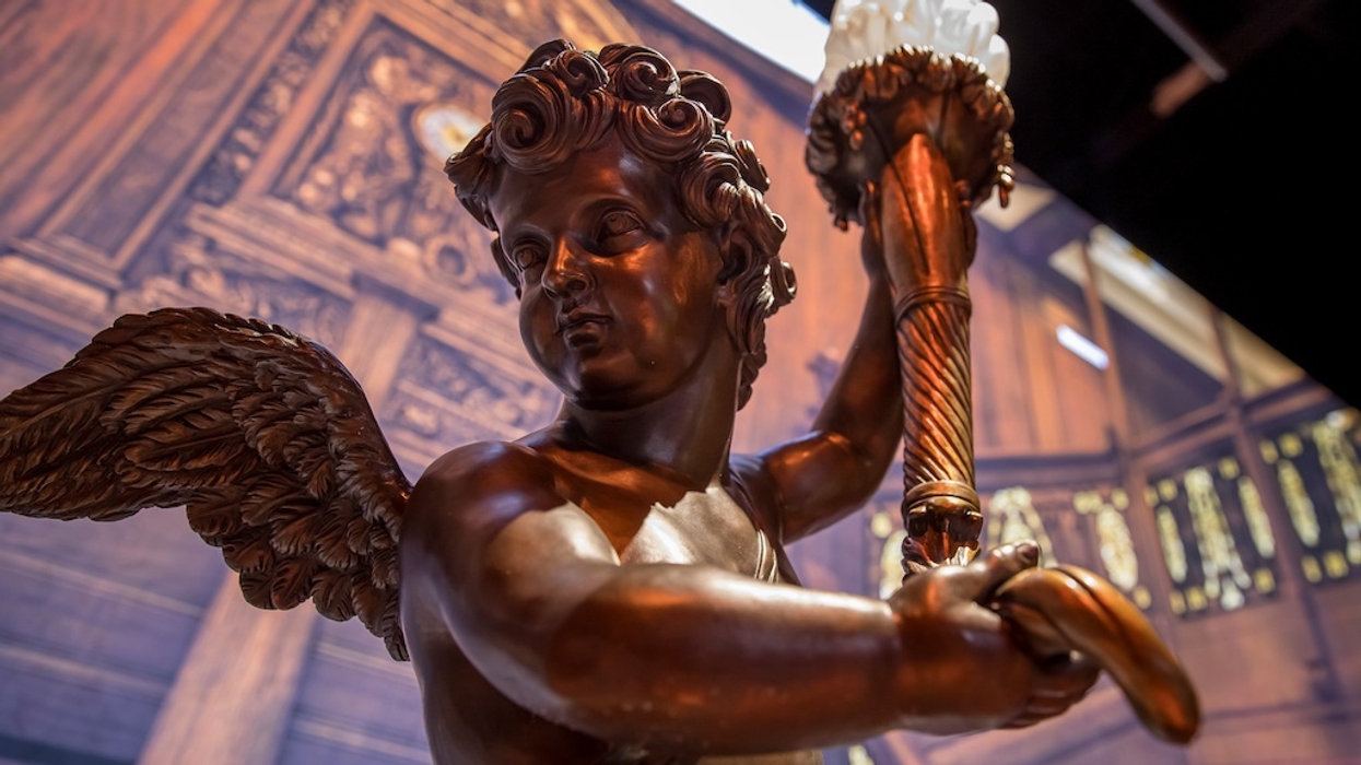 Bronze cherub statue holding a decorative lamp in an ornate wooden setting.
