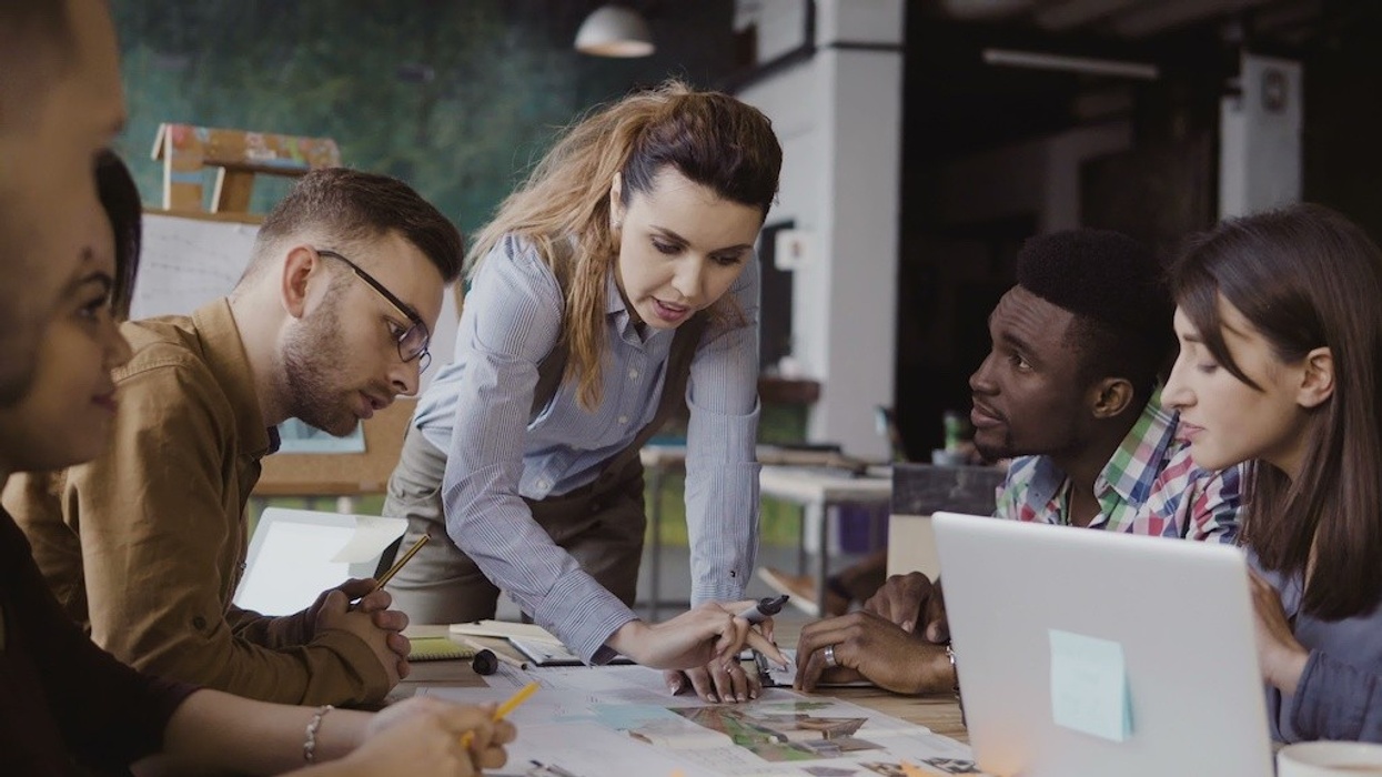 Brunette female team leader talking with mixed race group of people, writes with a marker on the model of house. Brainstorming of start-up company in modern office. Creative architectural project.