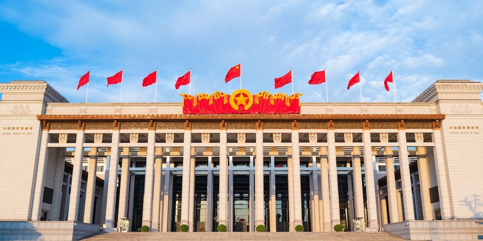 Building with red flags and decorative emblem under a blue sky.