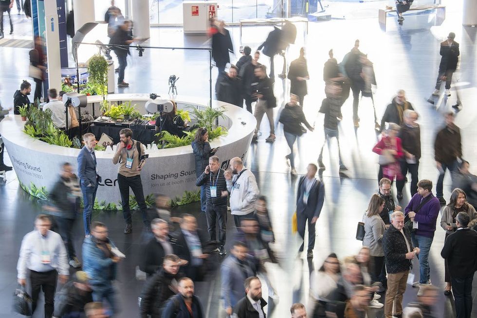 Busy event with people walking around a circular booth, plants and equipment visible.