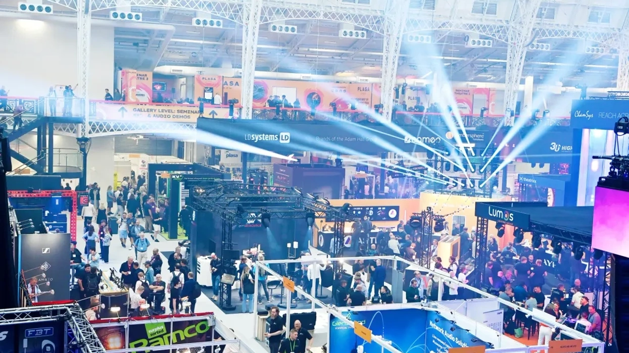 Busy trade show with booths, visitors, and bright overhead lights at PLASA