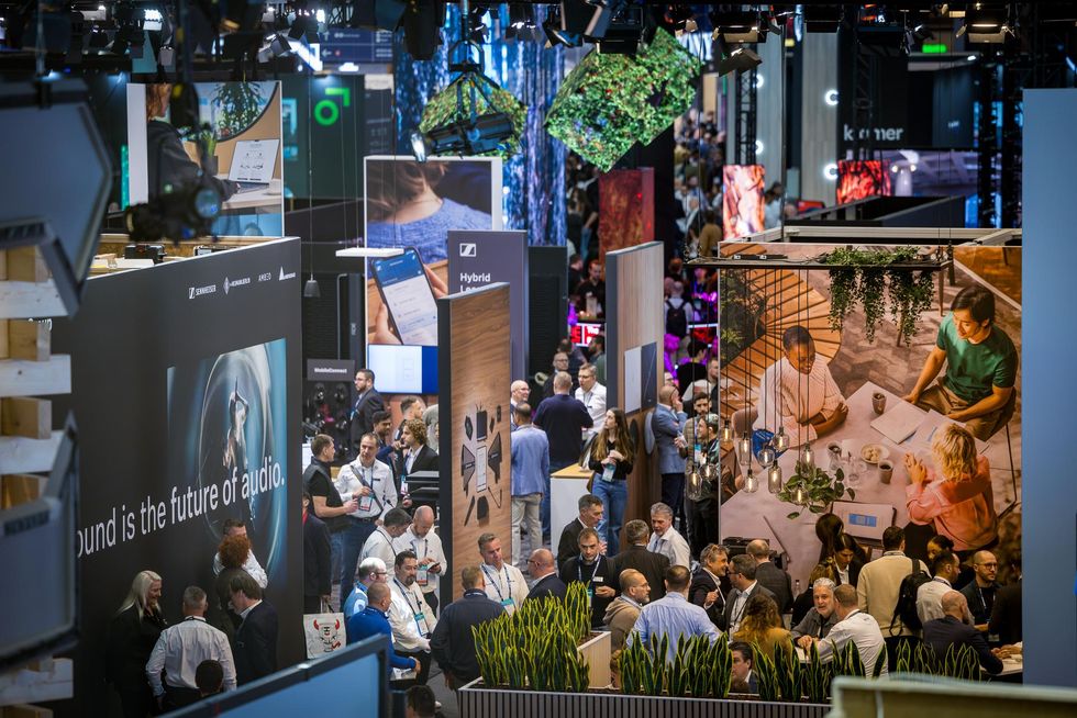 Busy trade show with people exploring audio and tech exhibits and large display images - ISE